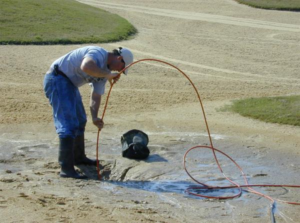 Jim Hill uses high-pressure water to clear clogged bunker drainage.